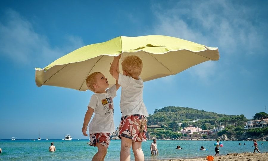 Schoolvakanties regio's in Nederland. Op de foto ter illustratie twee kinderen die een parasol opzetten op het strand. Typisch vakantie tafereel